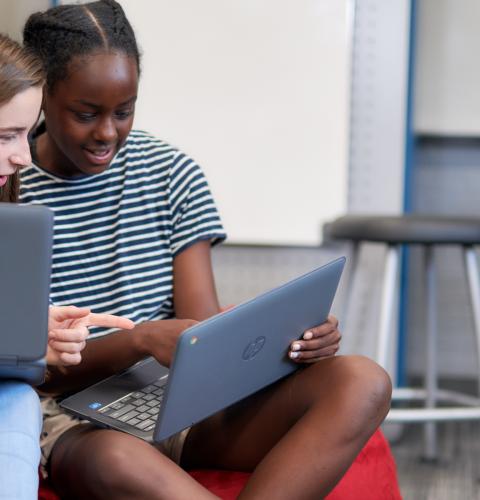 Two middle school students working on a laptop together.