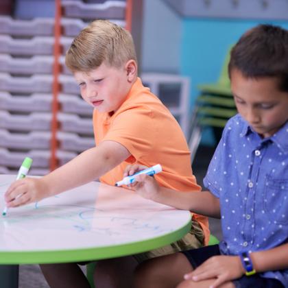 Two young boys drawing on a marker board table.