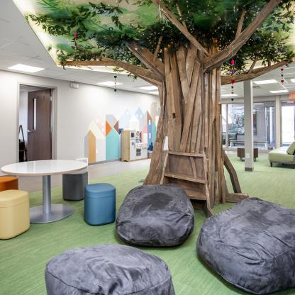 A room with a large tree sculpture, bean bag chairs, and colorful stools.