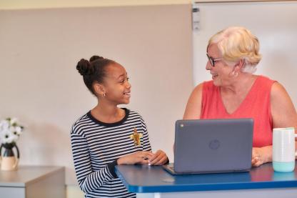 Student talking with teacher at desk.
