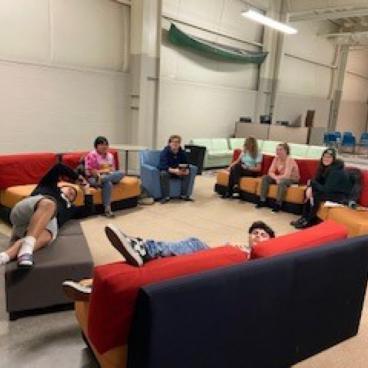 A group of teenagers lounging on sofas arranged in a circle.