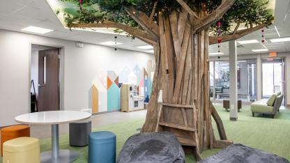 A room with a large tree sculpture, bean bag chairs, and colorful stools.