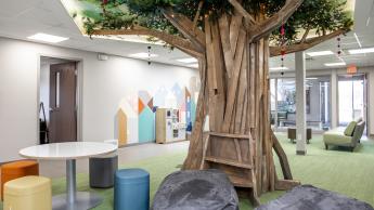 A room with a large tree sculpture, bean bag chairs, and colorful stools.